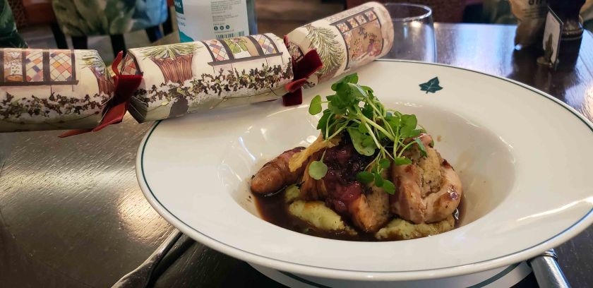 A plate of gourmet chicken dish with a rich sauce, garnished with microgreens, accompanied by a festive Christmas cracker in the background.