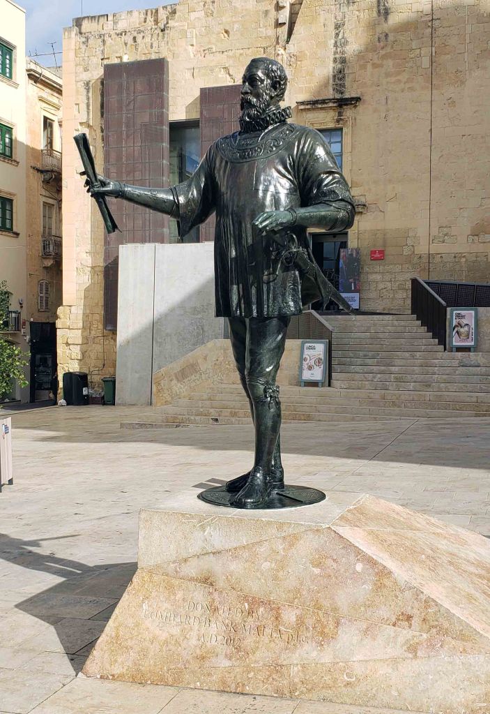 Bronze statue of a historical figure holding a scroll, located in front of a stone building.