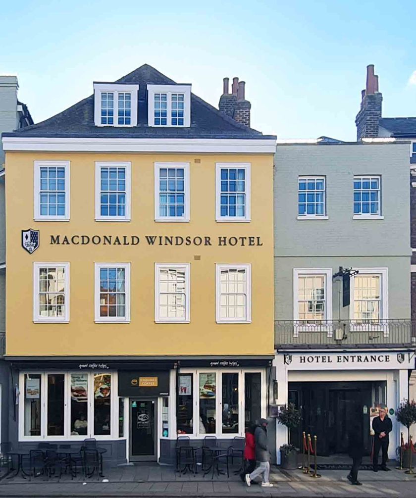 Exterior view of the Macdonald Windsor Hotel, showcasing a yellow facade with windows and the hotel entrance, set in a quaint street.